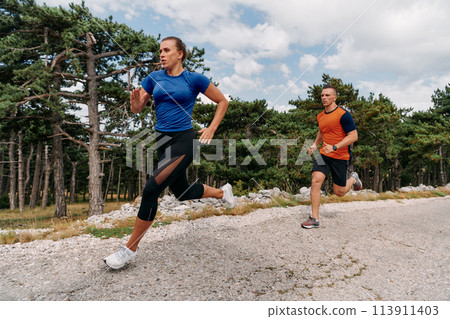 A couple dressed in sportswear runs along a scenic road during an early morning workout, enjoying the fresh air and maintaining a healthy lifestyle 113911403