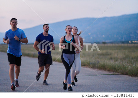 A diverse group of runners trains together at sunset. 113911435