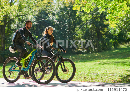 A blissful couple, adorned in professional cycling gear, enjoys a romantic bicycle ride through a park, surrounded by modern natural attractions, radiating love and happiness A blissful couple, adorned in professional cycling gear, enjoys a romantic bicycle ride through a park, surrounded by modern natural attractions, radiating love and happiness 113911470