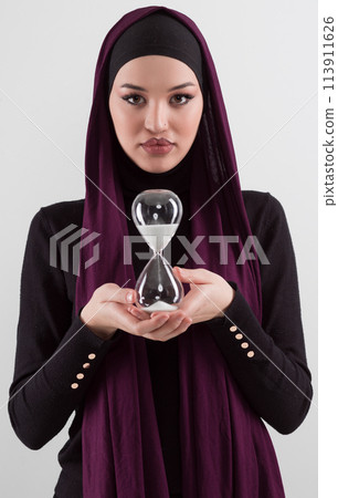 Beautiful arab businesswoman wearing hijab and holding sand clock. Time is passing and it's a pressure concept. Beautiful arab businesswoman wearing hijab and holding sand clock. Time is passing and it's a pressure concept. 113911626