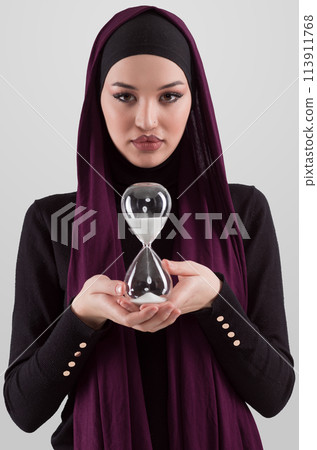Beautiful arab businesswoman wearing hijab and holding sand clock. Time is passing and it's a pressure concept. Beautiful arab businesswoman wearing hijab and holding sand clock. Time is passing and it's a pressure concept. 113911768