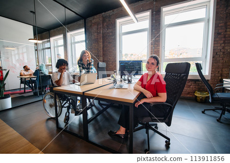 A diverse group of business professionals collaborates in a modern startup coworking center, utilizing a mix of paper-based and technological tools such as mobile phones and computers  113911856