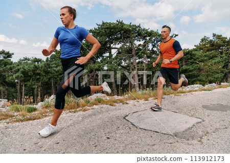 A couple dressed in sportswear runs along a scenic road during an early morning workout, enjoying the fresh air and maintaining a healthy lifestyle 113912173