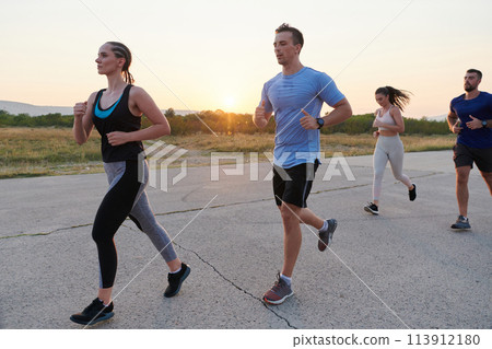 A diverse group of runners trains together at sunset. 113912180
