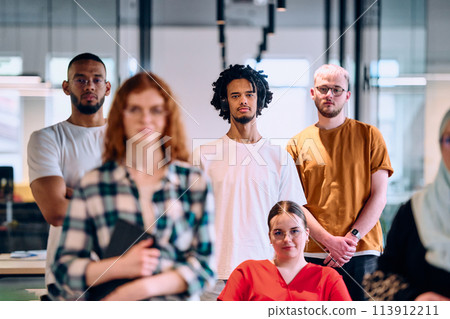 A diverse group of young business people walking a corridor in the glass-enclosed office of a modern startup, including a person in a wheelchair and a woman wearing a hijab 113912211