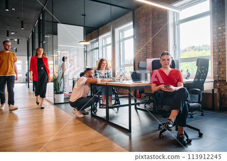 A diverse group of business professionals collaborates in a modern startup coworking center, utilizing a mix of paper-based and technological tools such as mobile phones and computers  113912245