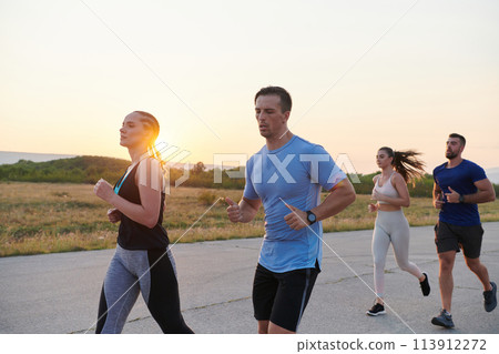 A diverse group of runners trains together at sunset. 113912272