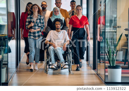 A diverse group of young business people congregates within a modern startup's glass-enclosed office, featuring inclusivity with a person in a wheelchair, an African American young man, and a hijab 113912322
