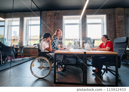 A diverse group of business professionals collaborates in a modern startup coworking center, utilizing a mix of paper-based and technological tools such as mobile phones and computers  113912433