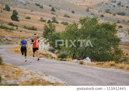 A couple dressed in sportswear runs along a scenic road during an early morning workout, enjoying the fresh air and maintaining a healthy lifestyle 113912441