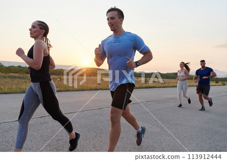 A diverse group of runners trains together at sunset. 113912444