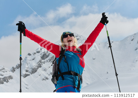 A professional woman skier rejoices after successfully climbing the snowy peaks of the Alps 113912517