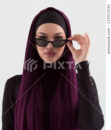 Portrait of beautiful stylish young muslim woman wearing black hijab and sunglasses as modern eastern fashion concept posing on white background. Portrait of beautiful stylish young muslim woman wearing black hijab and sunglasses as modern eastern fashion concept posing on white background. 113912542