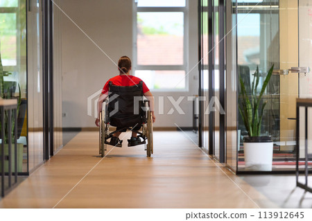 A modern young businesswoman in a wheelchair is surrounded by an inclusive workspace with glass-walled offices, embodying determination and innovation in the business world A modern young businesswoman in a wheelchair is surrounded by an inclusive workspace with glass-walled offices, embodying determination and innovation in the business world 113912645