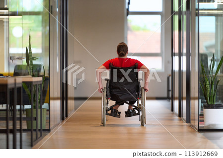 A modern young businesswoman in a wheelchair is surrounded by an inclusive workspace with glass-walled offices, embodying determination and innovation in the business world 113912669