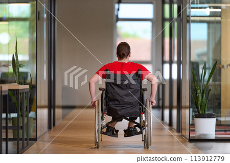 A modern young businesswoman in a wheelchair is surrounded by an inclusive workspace with glass-walled offices, embodying determination and innovation in the business world 113912779