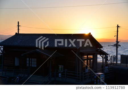 Sunset over a seaside hut. An old port house with the sun setting. A sea lodge bathed in the light of twilight. 113912780