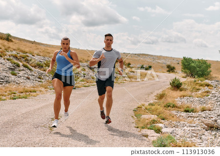 A couple dressed in sportswear runs along a scenic road during an early morning workout, enjoying the fresh air and maintaining a healthy lifestyle 113913036