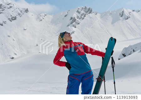 A professional woman skier rejoices after successfully climbing the snowy peaks of the Alps 113913093