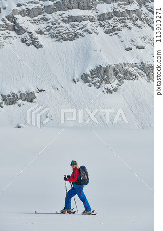 A female skier stands at the snowy summit of a mountain, equipped with professional gear and skis, poised for an exhilarating descent. 113913271