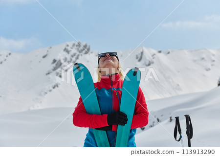 A professional woman skier rejoices after successfully climbing the snowy peaks of the Alps 113913290