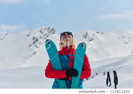 A professional woman skier rejoices after successfully climbing the snowy peaks of the Alps 113913291