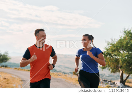 A couple dressed in sportswear runs along a scenic road during an early morning workout, enjoying the fresh air and maintaining a healthy lifestyle 113913645
