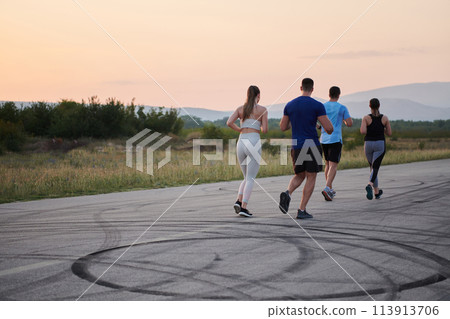 A diverse group of runners trains together at sunset. 113913706