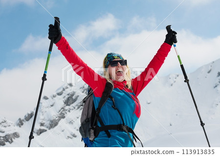 A professional woman skier rejoices after successfully climbing the snowy peaks of the Alps 113913835