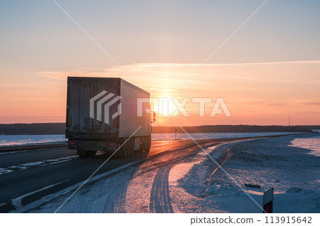 Semi truck driving along a snowy highway at sunset in winter 113915642