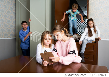 Two preteen girls trying to find solution of riddles in quest room 113917821