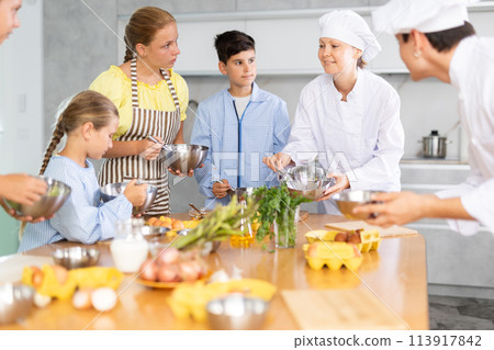Friendly female chef in white uniform giving culinary lesson to tweens 113917842