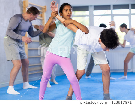 Black tween girl practicing armlock in training bout with boy during self defence course 113917871