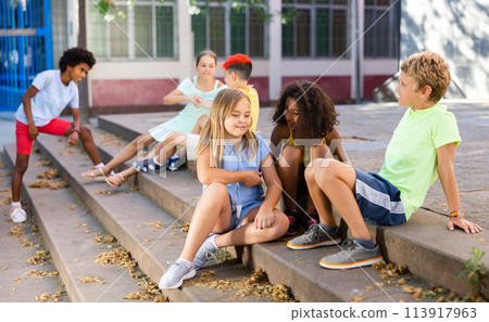 Group of boys and girls sitting on stairs outdoors and chatting 113917963