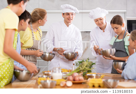 Young guy and adult woman cook teaches group of children to cook Young guy and adult woman cook teaches group of children to cook 113918033