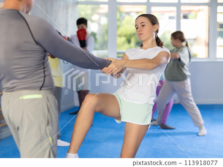 Teenage girl kicking instructor in groin during sparring at self-defense class 113918077