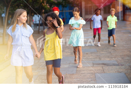 Two cheerful preteen girls enjoying walk along city street 113918184