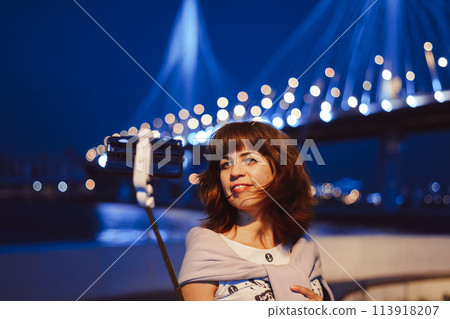 A girl takes pictures of herself on her phone at night in the city 113918207