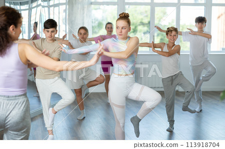 Female girl student repeats movements of unrecognizable teacher during group modern dance class. Female girl student repeats movements of unrecognizable teacher during group modern dance class. 113918704