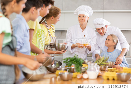 Positive professional chefs in white uniform conducting culinary masterclass for tweens Positive professional chefs in white uniform conducting culinary masterclass for tweens 113918774