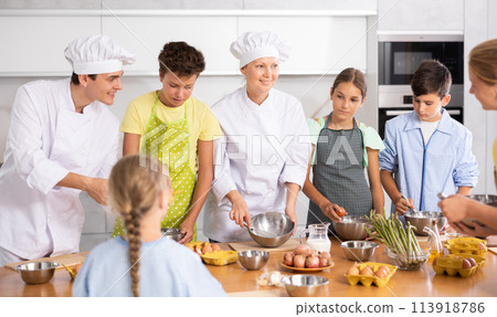 Young guy and adult woman cook teaches group of children to cook Young guy and adult woman cook teaches group of children to cook 113918786
