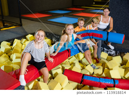 Happy tween children with woman sitting on soft beam above foam pit 113918814