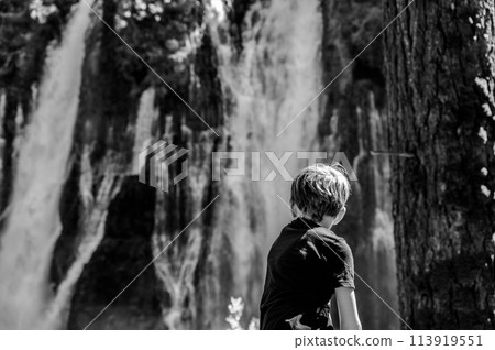 Boy looking out at McArthur-Burney Falls Memorial State Park cascading waterfall over a rock wall. Boy looking out at McArthur-Burney Falls Memorial State Park cascading waterfall over a rock wall. 113919551