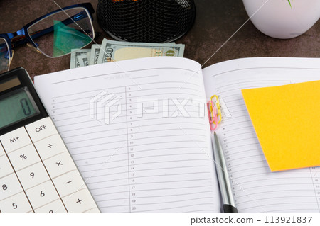 The notebook is open for urgent writing with a calculator, dollar bills and a pen in the composition. A place to copy 113921837