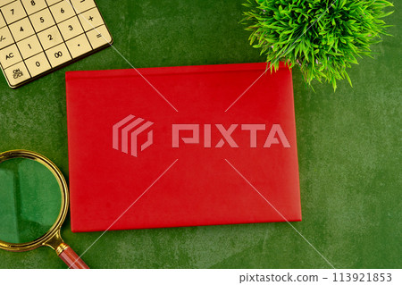 A magnifying glass, a calculator and a closed notebook with a great secret on a green surface. Mysterious atmosphere. A place to copy A magnifying glass, a calculator and a closed notebook with a great secret on a green surface. Mysterious atmosphere. A place to copy 113921853