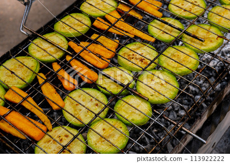 Chopped zucchini and carrots roasting on fire seasoned with aroma herbs and spices. Delicious fresh vegetables grilling on barbecue smoker grid. Diet vegan bbq. Outdoor recreation Chopped zucchini and carrots roasting on fire seasoned with aroma herbs and spices. Delicious fresh vegetables grilling on barbecue smoker grid. Diet vegan bbq. Outdoor recreation 113922222