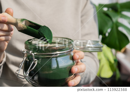 Female hands holding Organic blue-green algae spirulina detox powder in glass jar. Health protein of chlorella. Vitamins and minerals to diet. Prebiotic and antioxidant rich Dietary supplement Seaweed Female hands holding Organic blue-green algae spirulina detox powder in glass jar. Health protein of chlorella. Vitamins and minerals to diet. Prebiotic and antioxidant rich Dietary supplement Seaweed 113922388