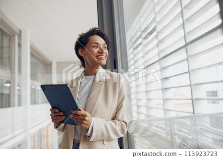 Pretty female manager with digital tablet standing on modern office background and looks away 113923723