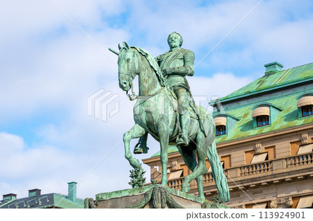 The statue of Gustav II Adolf is captured here standing proudly in Stockholm, Sweden, with clear skies and surrounded by the city architecture. 113924901