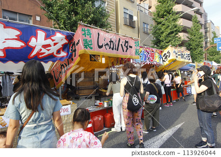 The festival stalls continue all the way to the traffic lights at the closed intersection. People happily walk around looking at the stalls and eating. 113926044